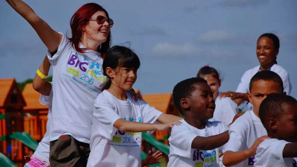 A group of children and a supervising adult participate in an outdoor activity on the longest swing set, all wearing matching event t-shirts.