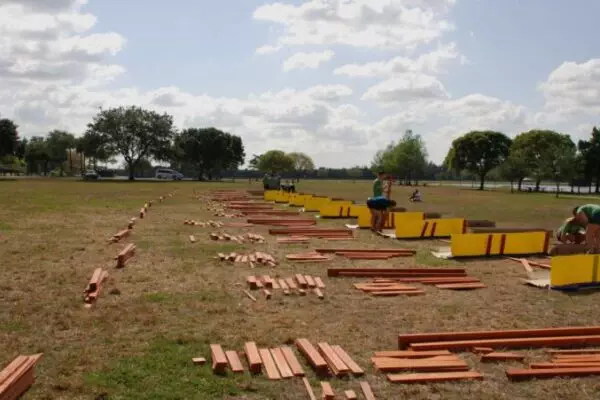 People are assembling the longest swing set on a grassy field under a partly cloudy sky. Various wooden pieces and materials are laid out on the ground, contributing to this impressive build.